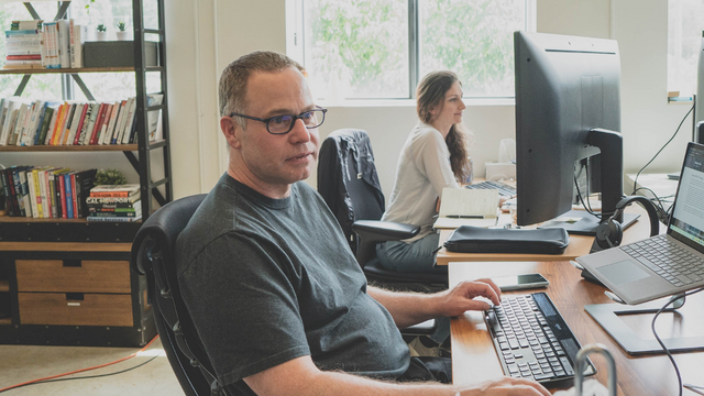 Picture of two coworkers sitting at their desks working in front of computers