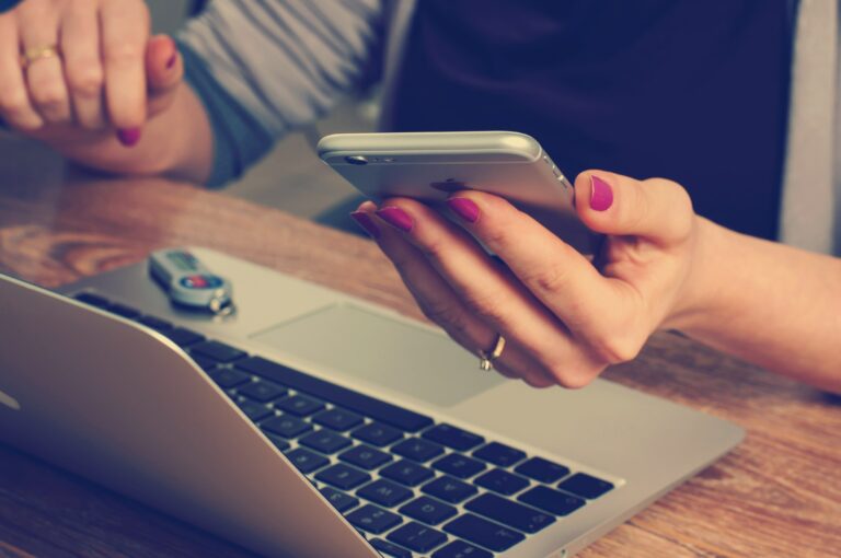 Woman at desk with her laptop open in front of her while she checks her phone